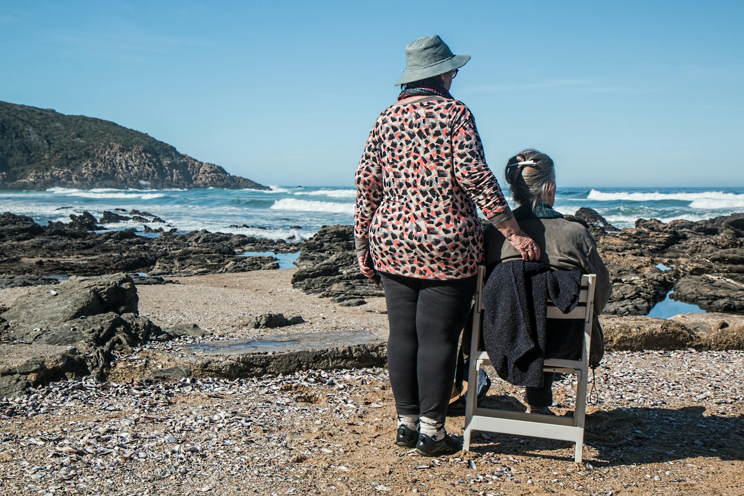 Two senior women enjoying a peaceful moment by the rocky beach, embracing friendship and serenity.